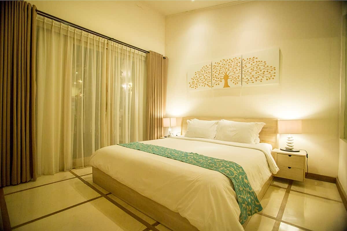 A hotel room with a large bed, a nightstand with a lamp, and a wall-mounted artwork of a tree.