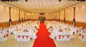 Una sala da banchetto con tavoli rotondi disposti a file, una passerella con tappeto rosso e un palco di fronte.