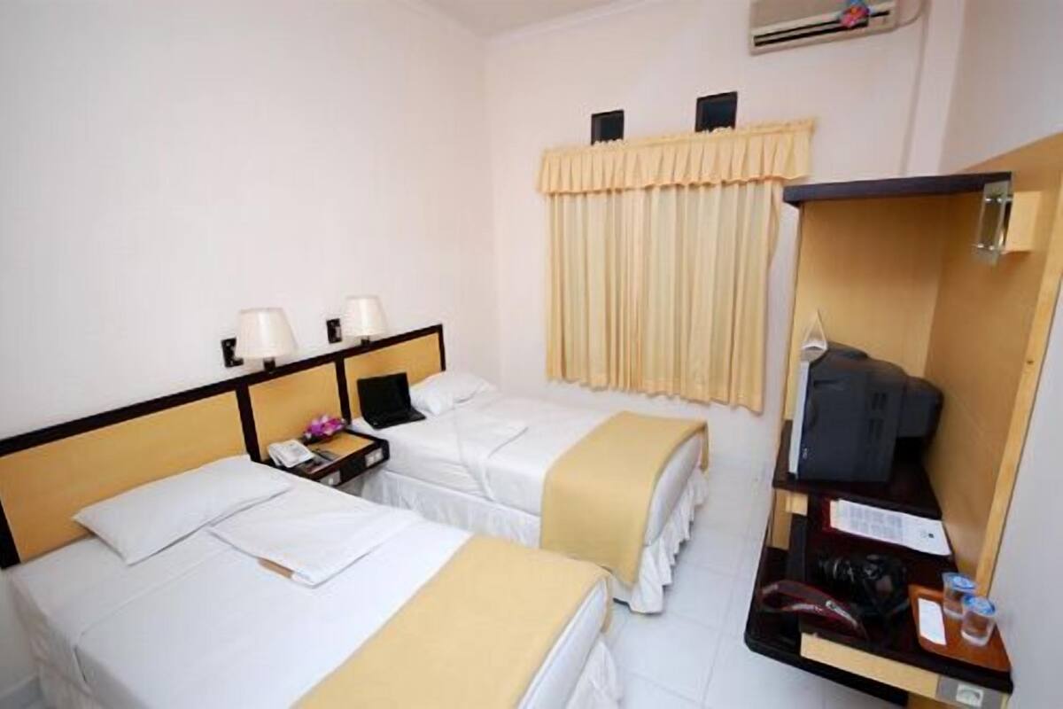 A hotel room with two beds, a desk, a chair, and a wardrobe.