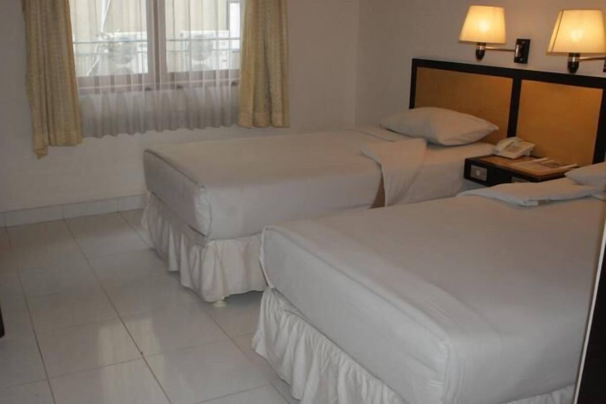 A hotel room with two beds, a TV, and a nightstand with a lamp.