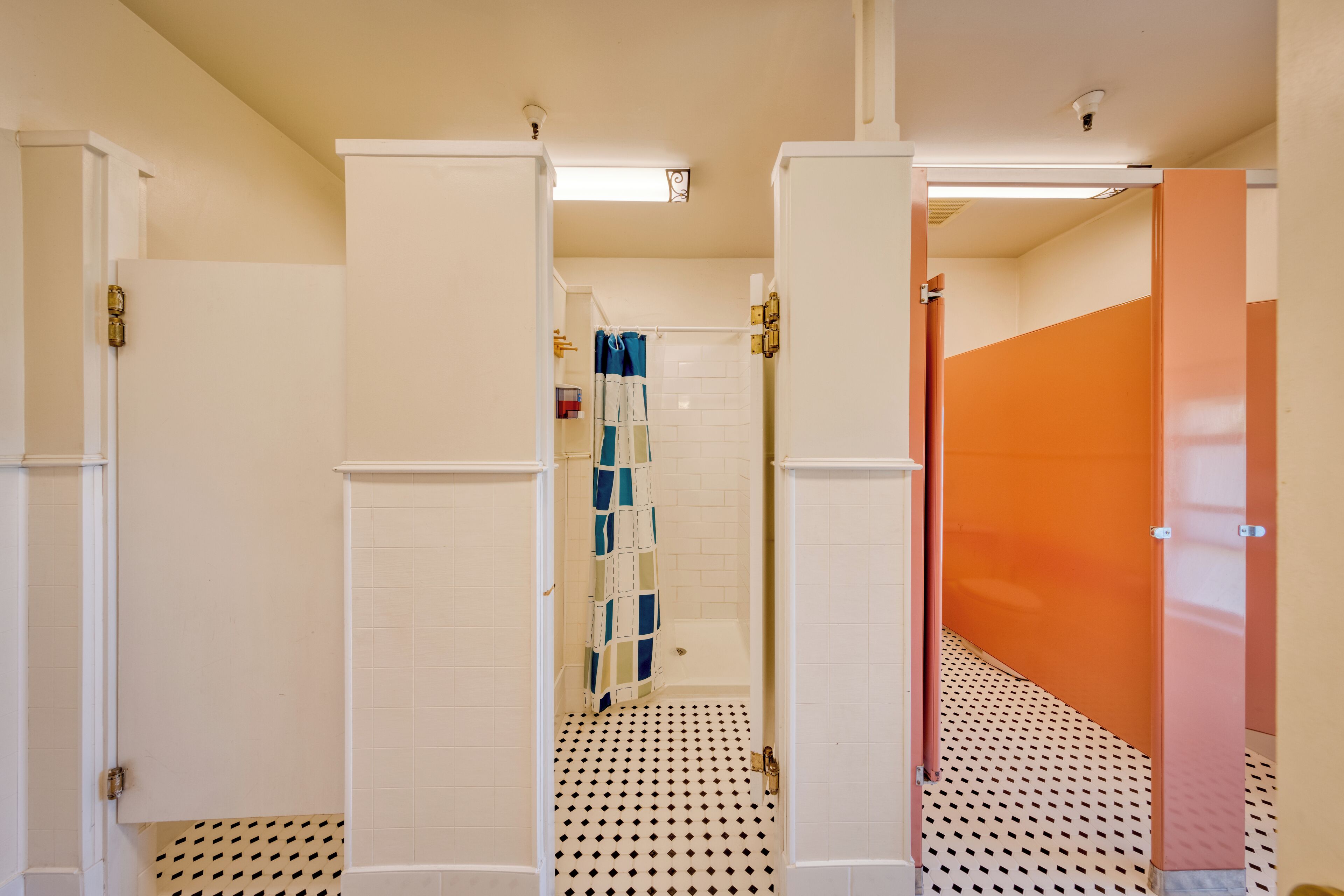 Un baño con paredes blancas, piso de baldosas y zona de ducha con cortina azul.