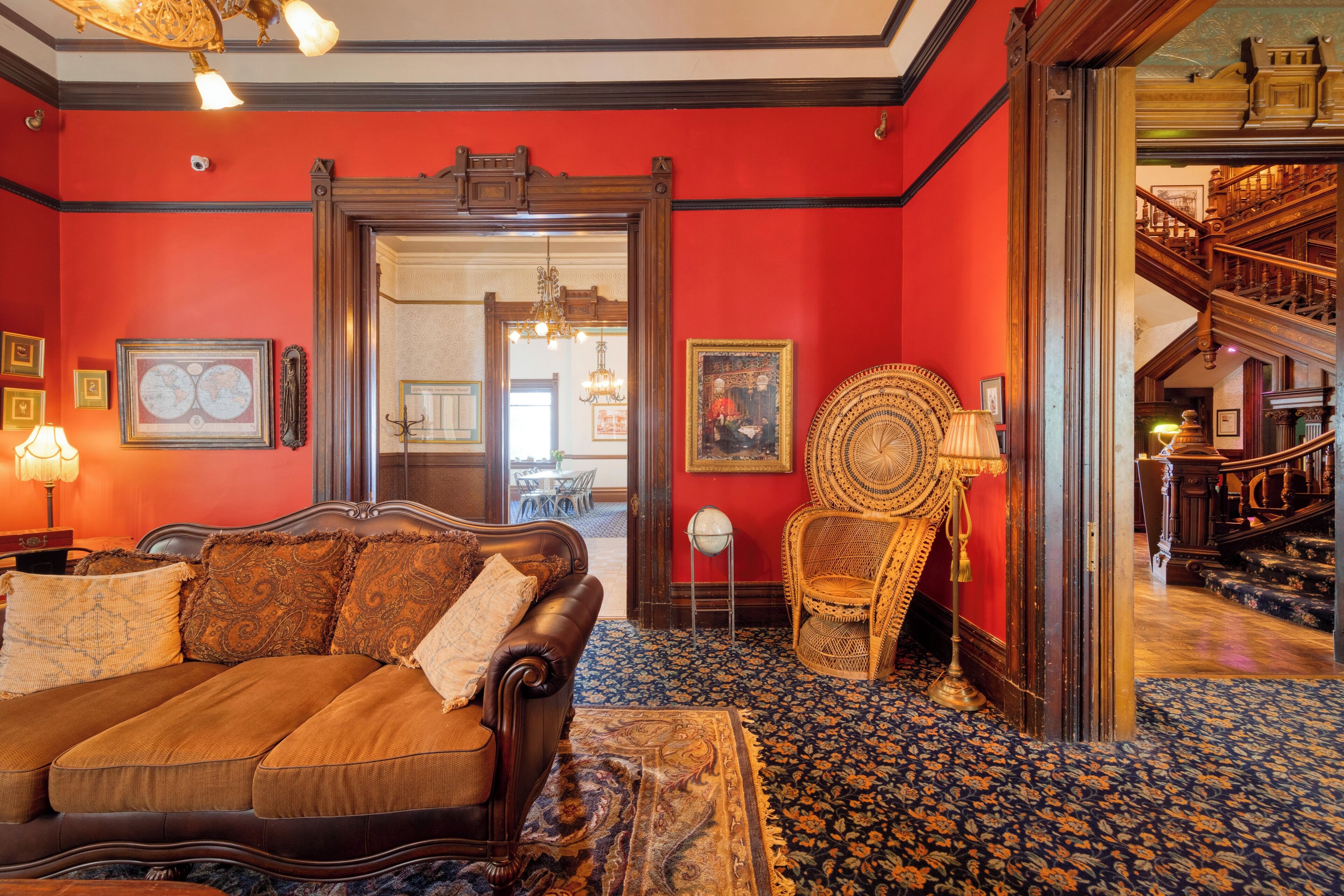 A room with a red wall, a brown sofa, a patterned rug, and a wooden chair.