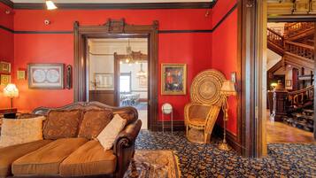 A room with a red wall, a brown sofa, a patterned rug, and a wooden chair.