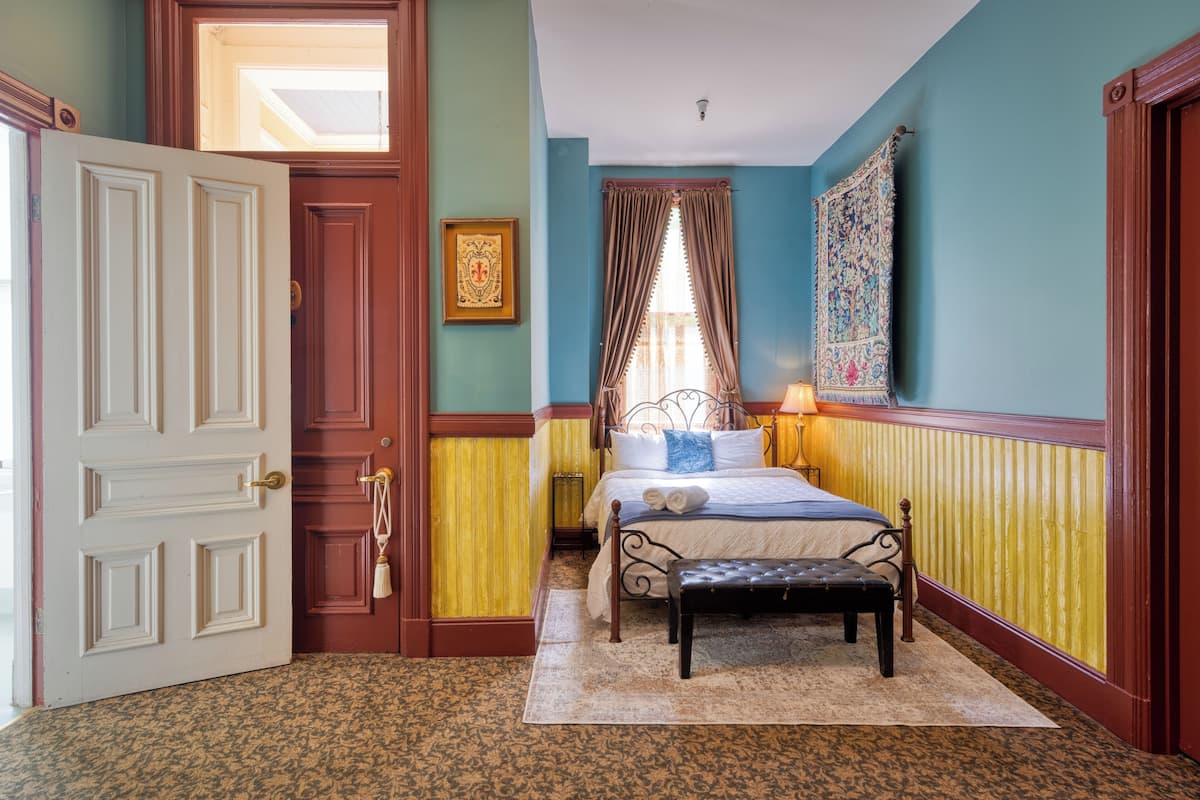 Ein Schlafzimmer mit Bett, einer Bank, einer Tür und einem Fenster mit Vorhängen.
