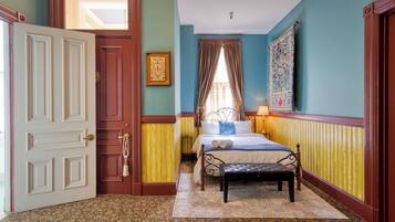 Un dormitorio con cama, un banco, una puerta y una ventana con cortinas.