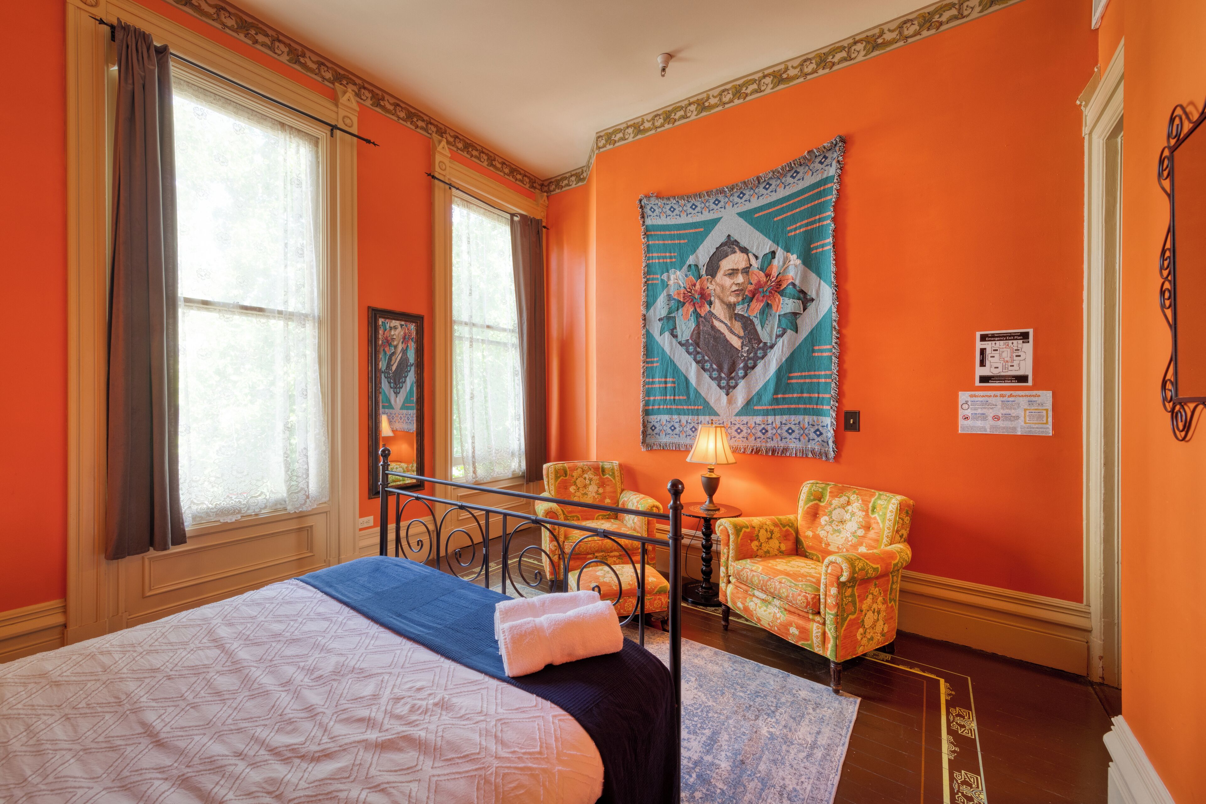 Une chambre d’hôtel avec un grand lit, deux chaises, une table et une tapisserie au mur.