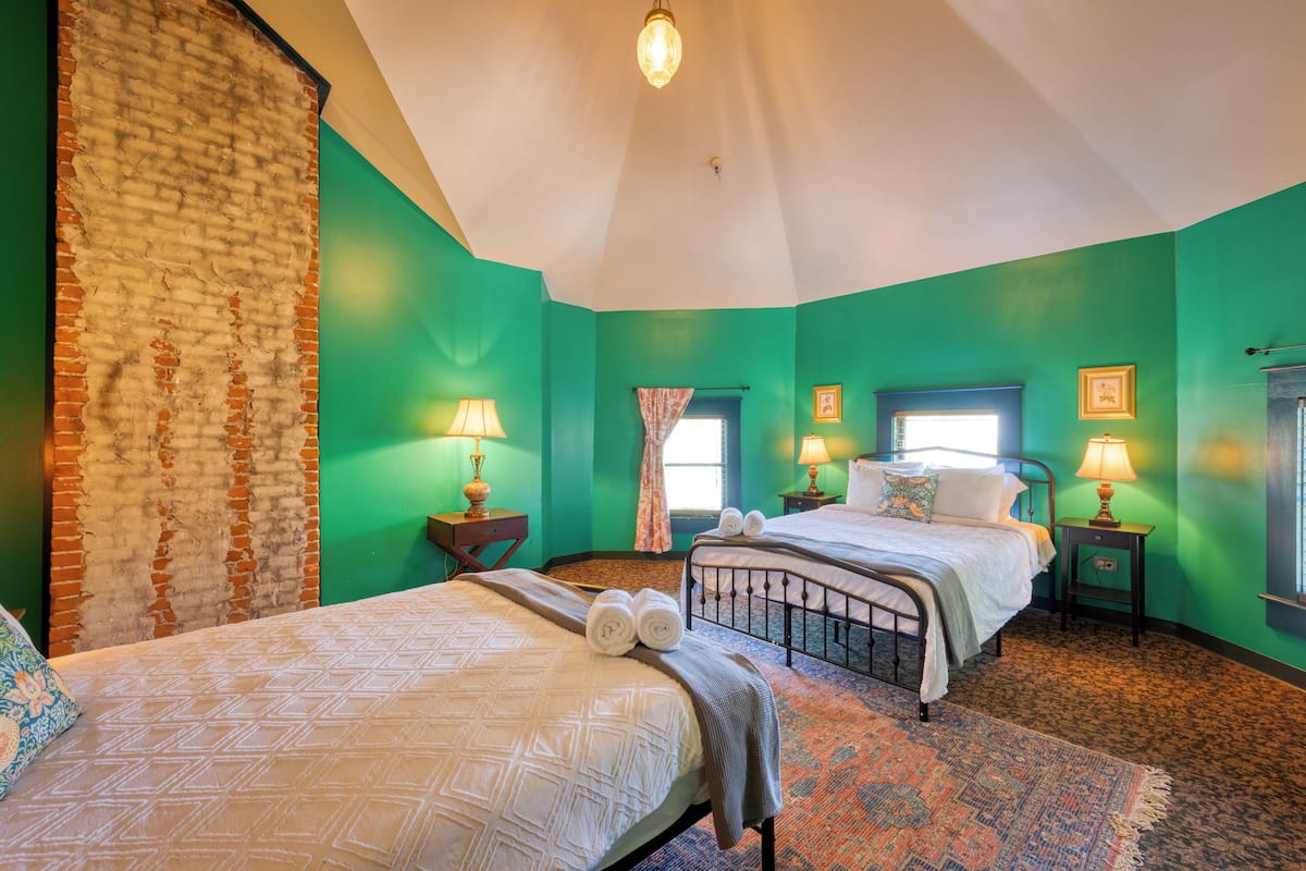 Ein Zimmer mit zwei Betten, grünen Wänden, einer Ziegelwand und einem gemusterten Teppich.