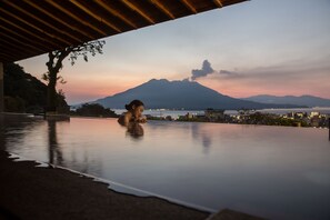 Una persona descansando junto a una piscina que refleja un paisaje montañoso y una vista urbana.