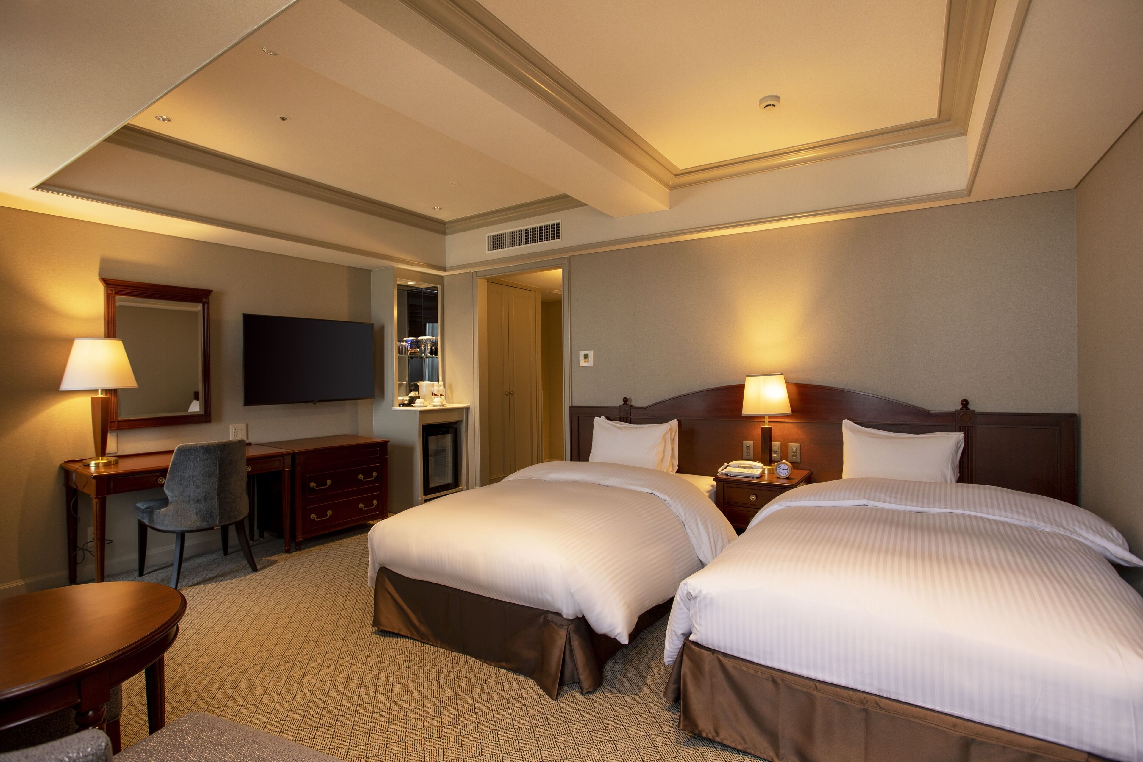Une chambre d’hôtel avec deux lits, un bureau, une chaise, une télévision et un miroir.