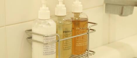 A bathroom shelf with three bottles of Provins lavender conditioner, Provins shower gel, and Provins almond shower gel.