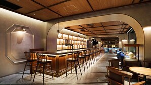 Een bar met houten stoelen en tafels, een lange toonbank en planken met flessen.