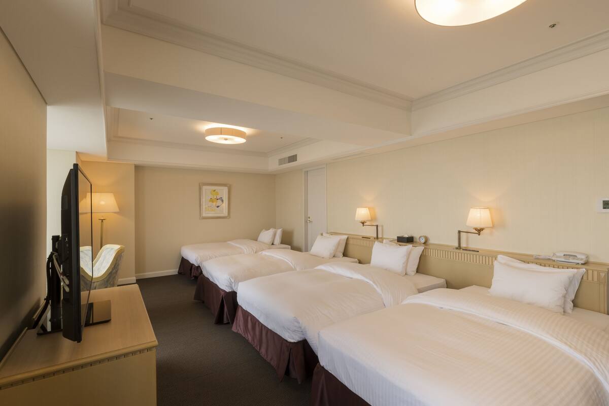 A hotel room with three single beds, a desk with a flat-screen TV, and a mirror.