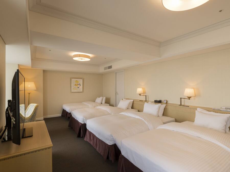 Ein Hotelzimmer mit drei Einzelbetten, einem Schreibtisch und einem Flachbildfernseher sowie einem Spiegel.