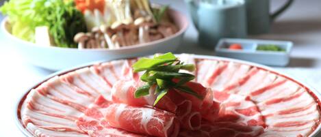 A plate of thinly sliced meat garnished with green leaves, a bowl of assorted vegetables, and a teapot in the background.