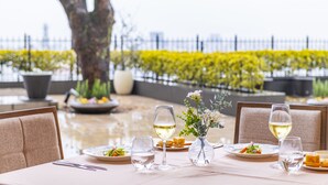 Een eettafel gedekt met borden, glazen en een vaas met bloemen, met uitzicht op een bloemenbed in geel.