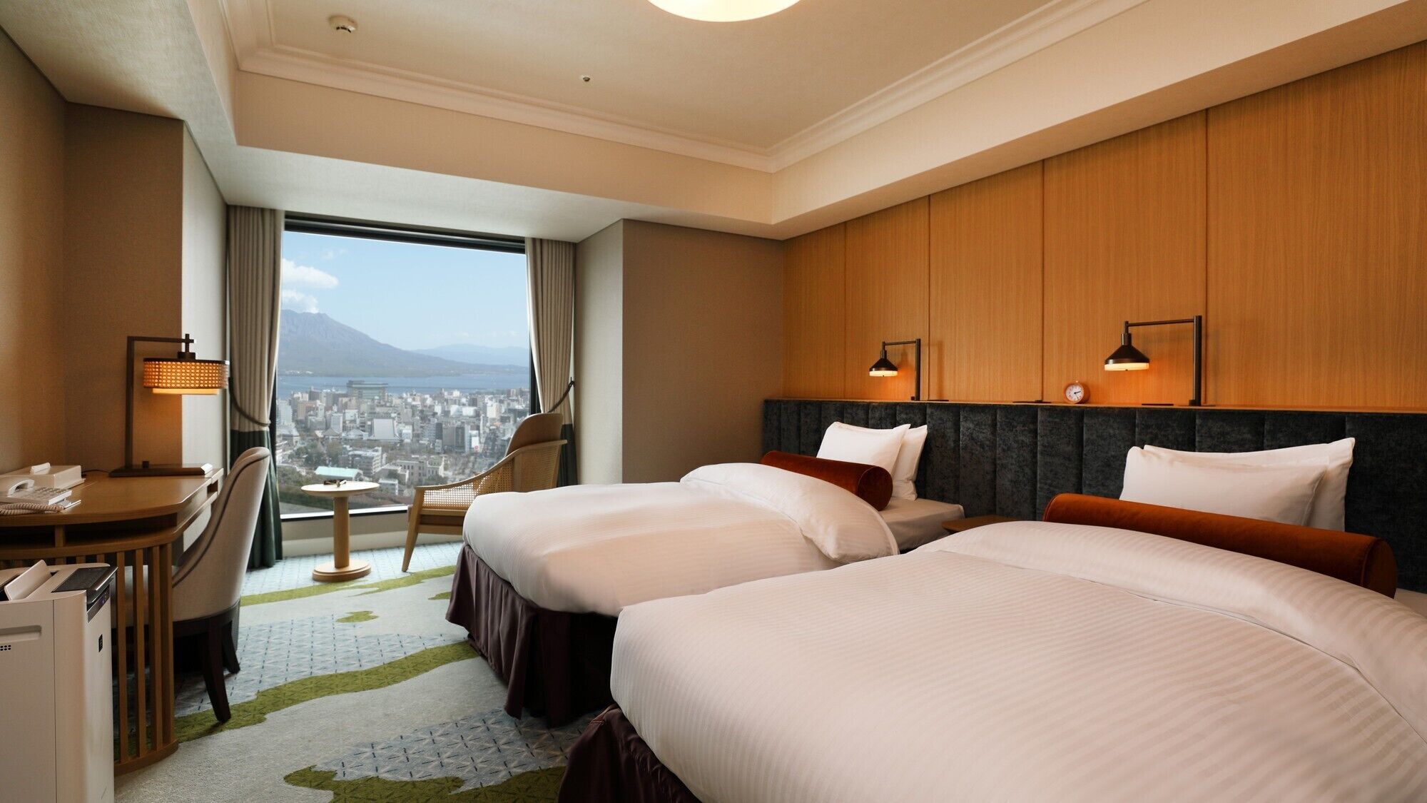 Ein Hotelzimmer mit zwei Betten, einem Schreibtisch, einem Stuhl und Blick auf die Stadt.