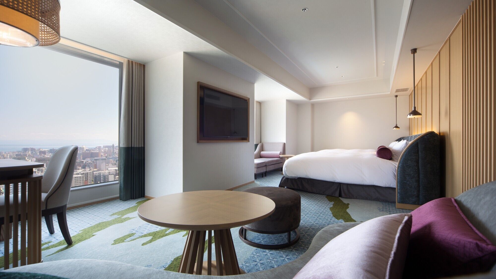 Ein Hotelzimmer mit großem Fenster, einem Bett, einem Sofa, einem Tisch und einem Fernseher.