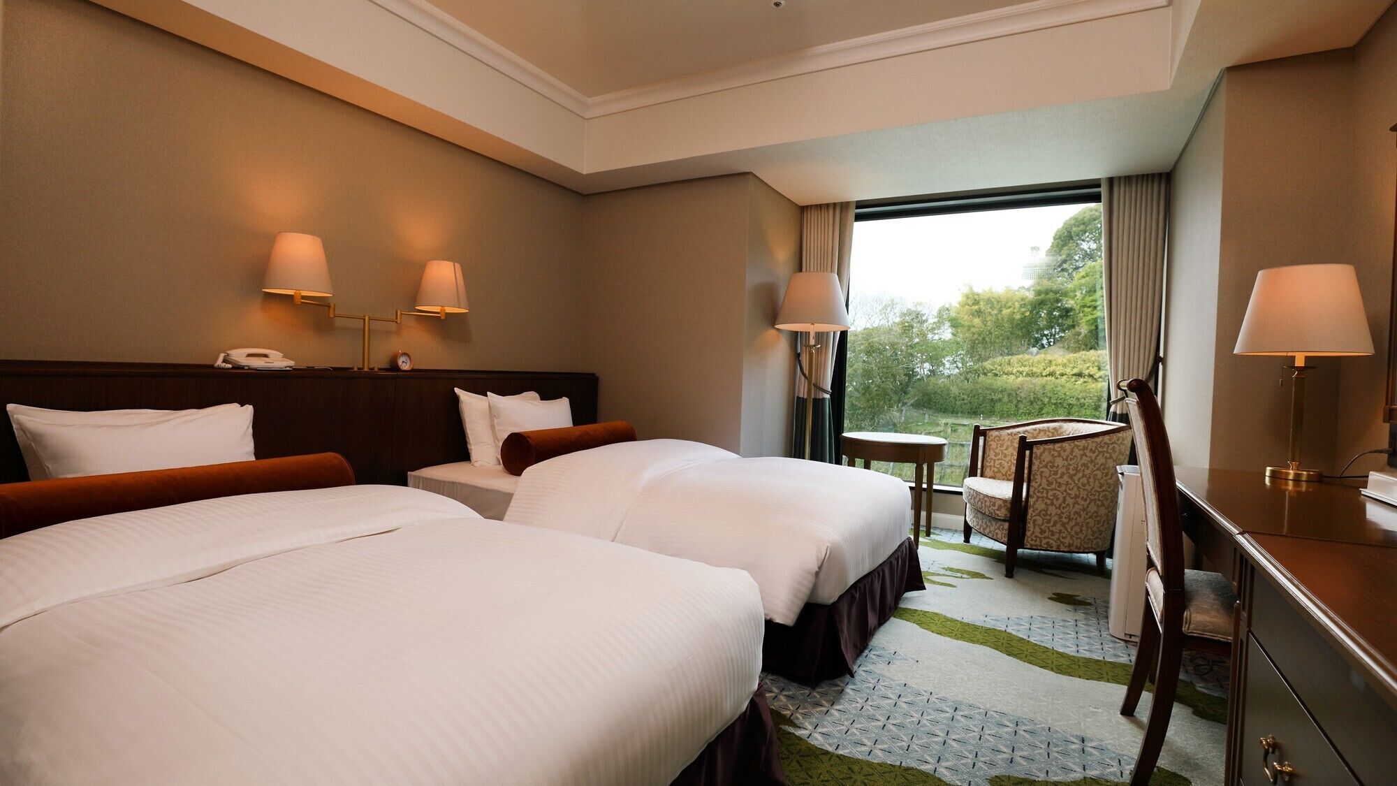 Ein Hotelzimmer mit zwei Betten, einem Schreibtisch, einem Stuhl und Blick ins Freie.