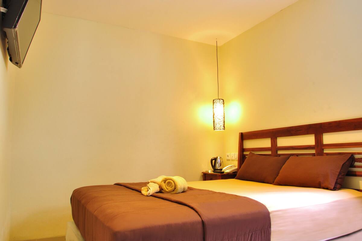 A hotel room with a neatly made bed, a bedside table with a lamp, and a wall-mounted television.