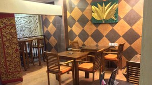 A restaurant with a patterned wall, wooden furniture, and a decorative panel. - Kuta Sari House (Kuta)