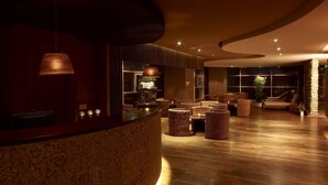 A modern lobby with a curved reception desk, wicker furniture, and a stone accent wall. - Cocor Spa Hotel (Neptun)