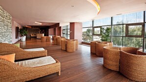 A spacious lobby with wicker furniture, large windows, and a stone wall. - Cocor Spa Hotel (Neptun)