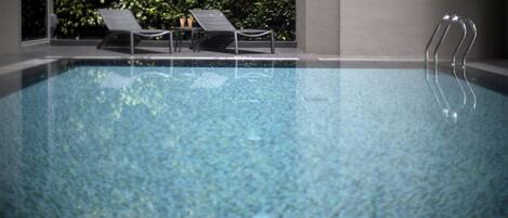 Una piscina con sillas de descanso y una escalera metálica.