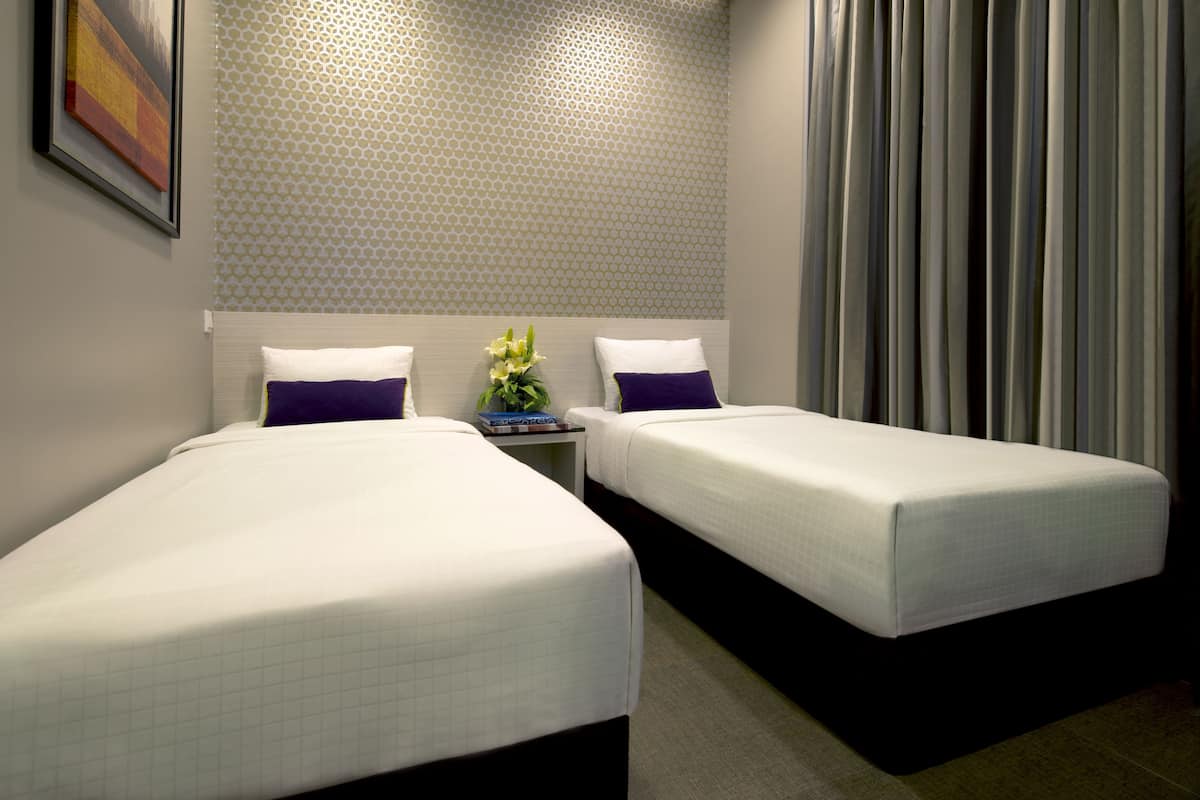Une chambre d’hôtel avec deux lits simples, une table de chevet ornée d’un vase de fleurs et un mur à motifs.