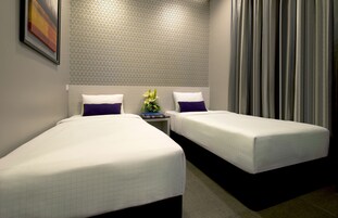 Habitación de hotel con dos camas individuales, una mesita de noche con un jarrón de flores y un papel tapiz estampado.