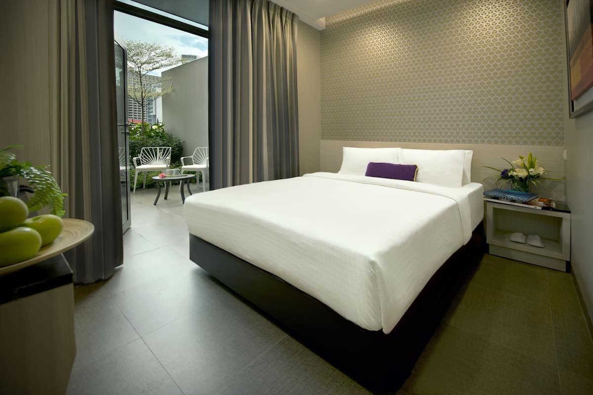 Une chambre d’hôtel moderne avec un grand lit, une petite table de chevet, une chaise et une vue sur l’extérieur.