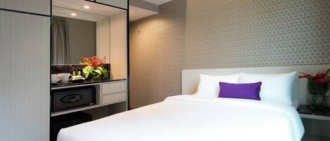 A hotel room with a large bed, a desk with a computer, a mirror, and a wall with a geometric pattern.
