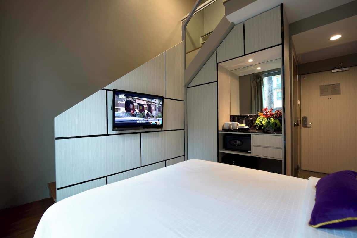 Une chambre d’hôtel comprenant un lit, un téléviseur fixé au mur, une petite kitchenette et une salle de bain avec un miroir.