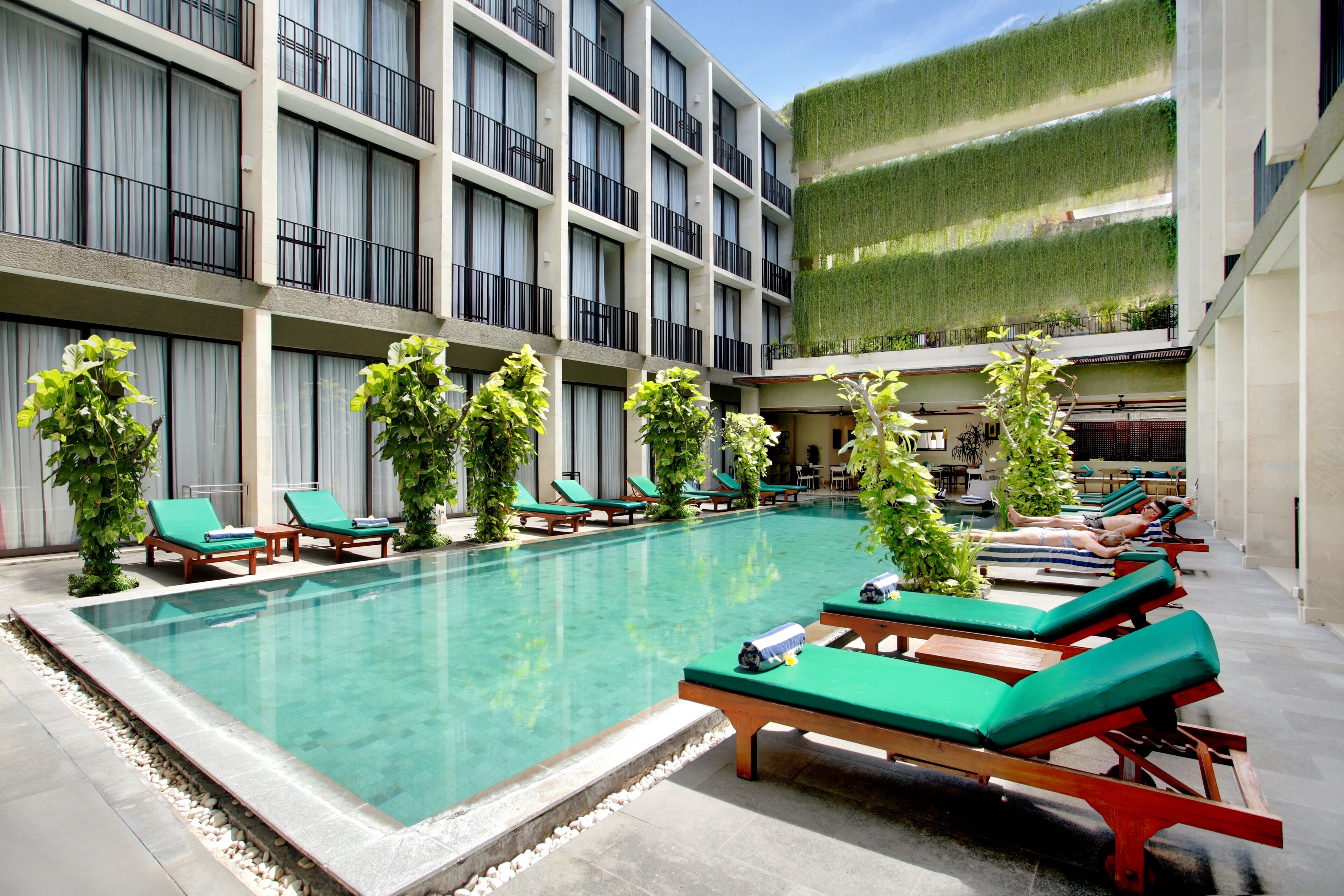 Zona de piscina con sillas de descanso y un edificio con balcones.