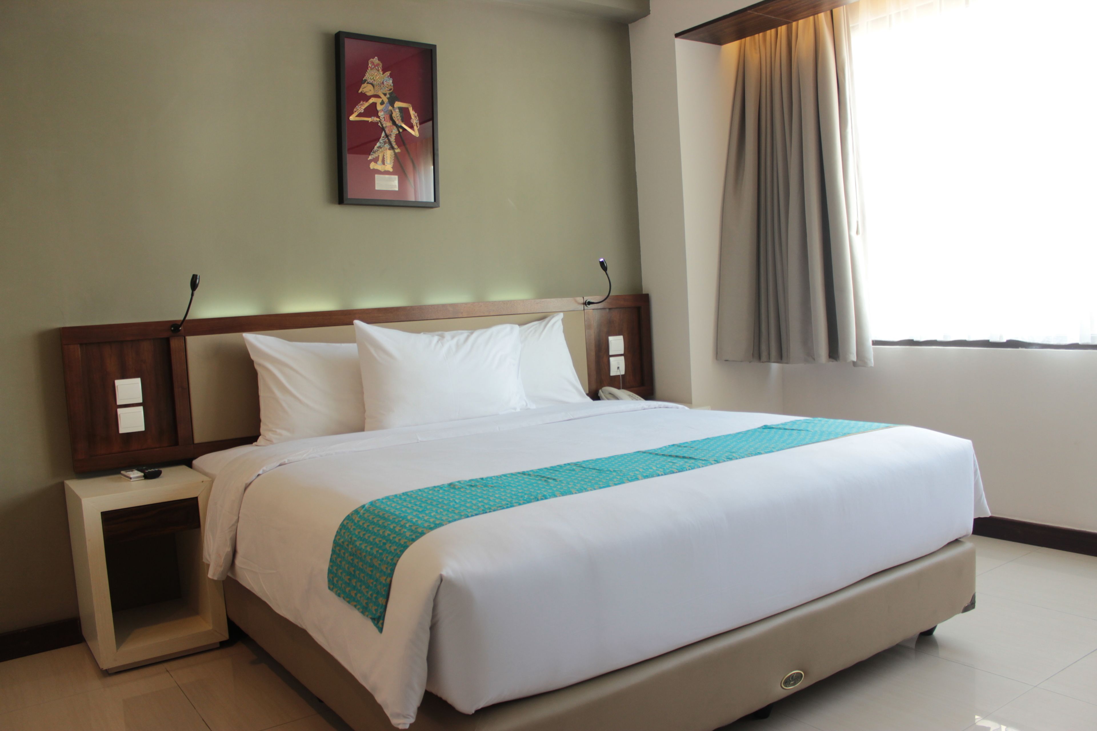 A hotel room with a large bed, a nightstand, a bedside table, a wall-mounted telephone, and a window with curtains.