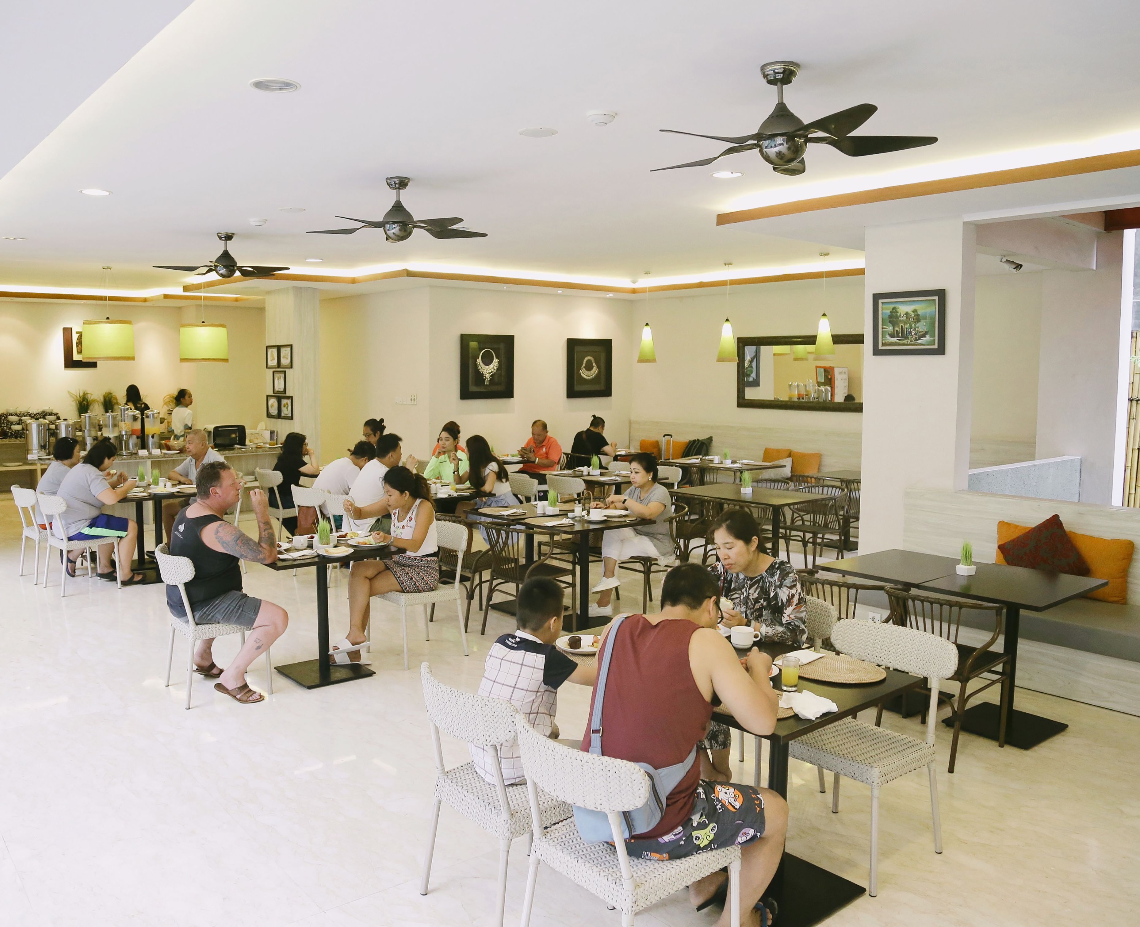 A spacious dining area with multiple tables and chairs, ceiling fans, and wall-mounted lights.