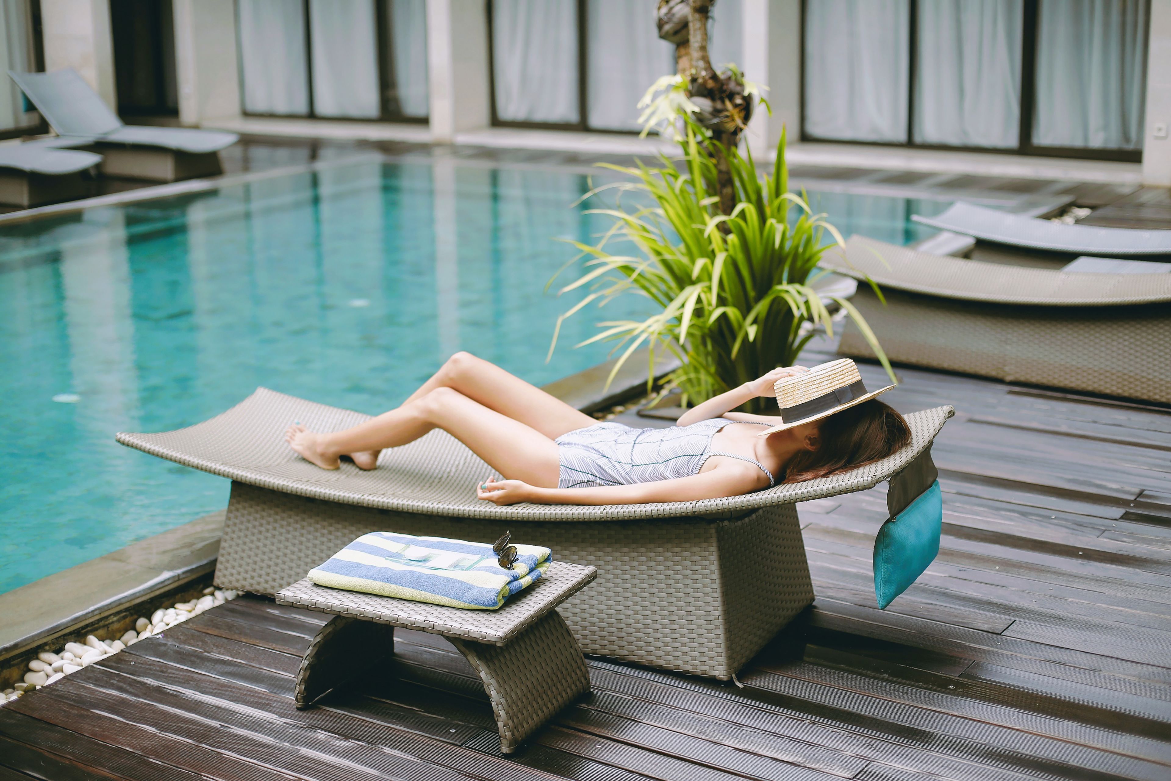 A poolside lounge area with a reclining chair, a small table with a towel, and a potted plant.
