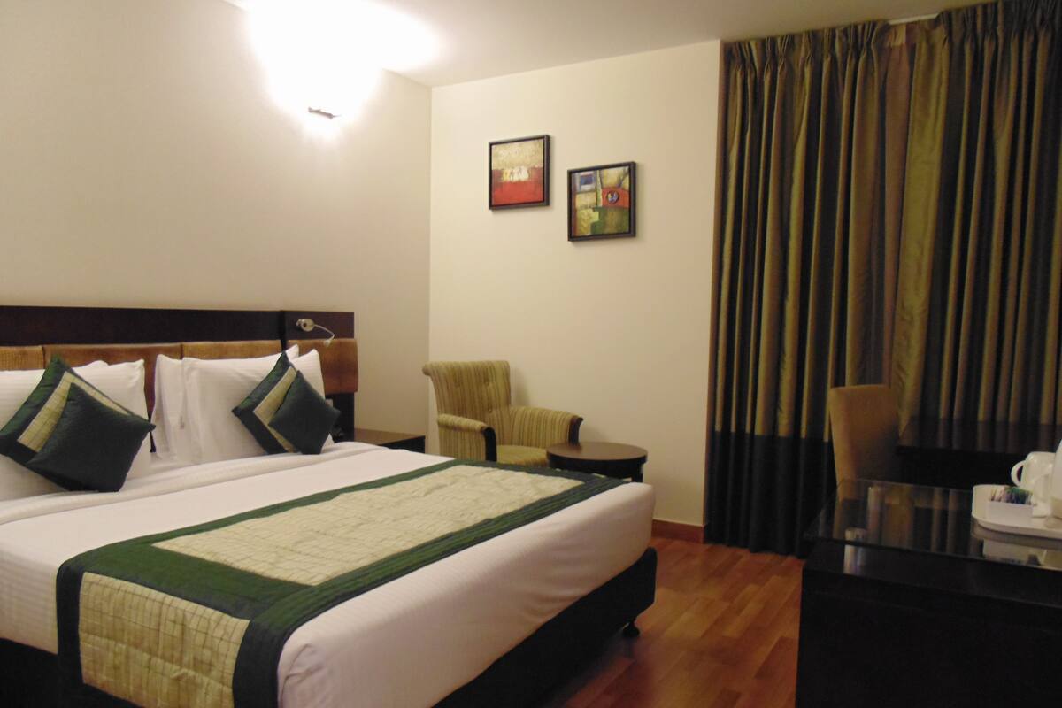 A hotel room with a large bed, a chair, a small table, and two framed pictures on the wall.