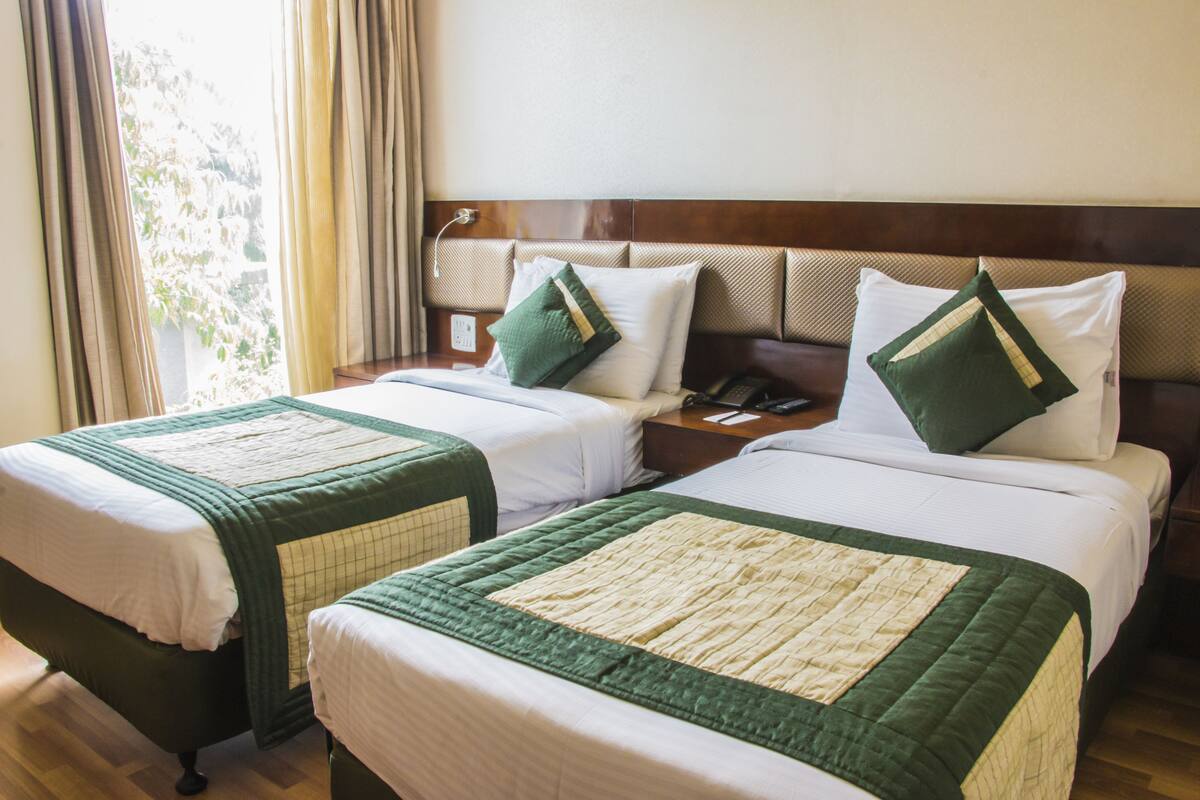 Two adjacent beds with green and white bedding, a wooden headboard, and a bedside table with a phone and a lamp.