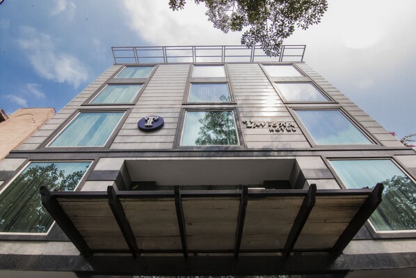 A modern building with a prominent 'T' logo, large windows, and a balcony area. - Tavisha Hotel (New Delhi)
