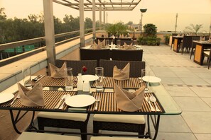 An outdoor dining area with tables set for two, featuring woven chairs and glass-top tables. - Tavisha Hotel (New Delhi)