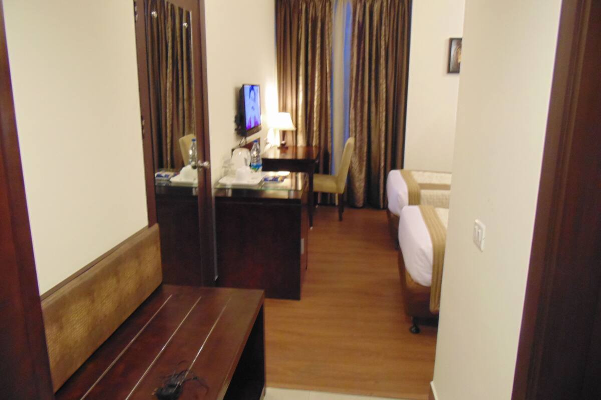 A hotel room with a wooden bench, a desk with a television, a chair, and a bed.