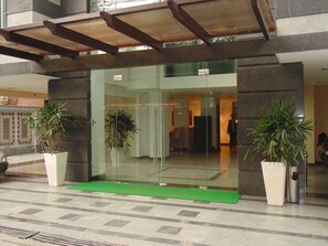 A hotel entrance with a glass door, potted plants, and a green mat. - Tavisha Hotel (New Delhi)