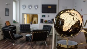 A globe on a stand in a room with a wooden floor, black chairs, and a TV on the wall.