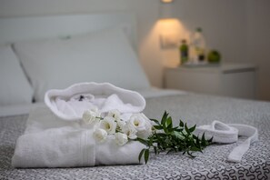 A neatly made bed with a white towel and a bouquet of white flowers on a patterned bedspread. - Hotel Forlanini52 Parma (Parma)