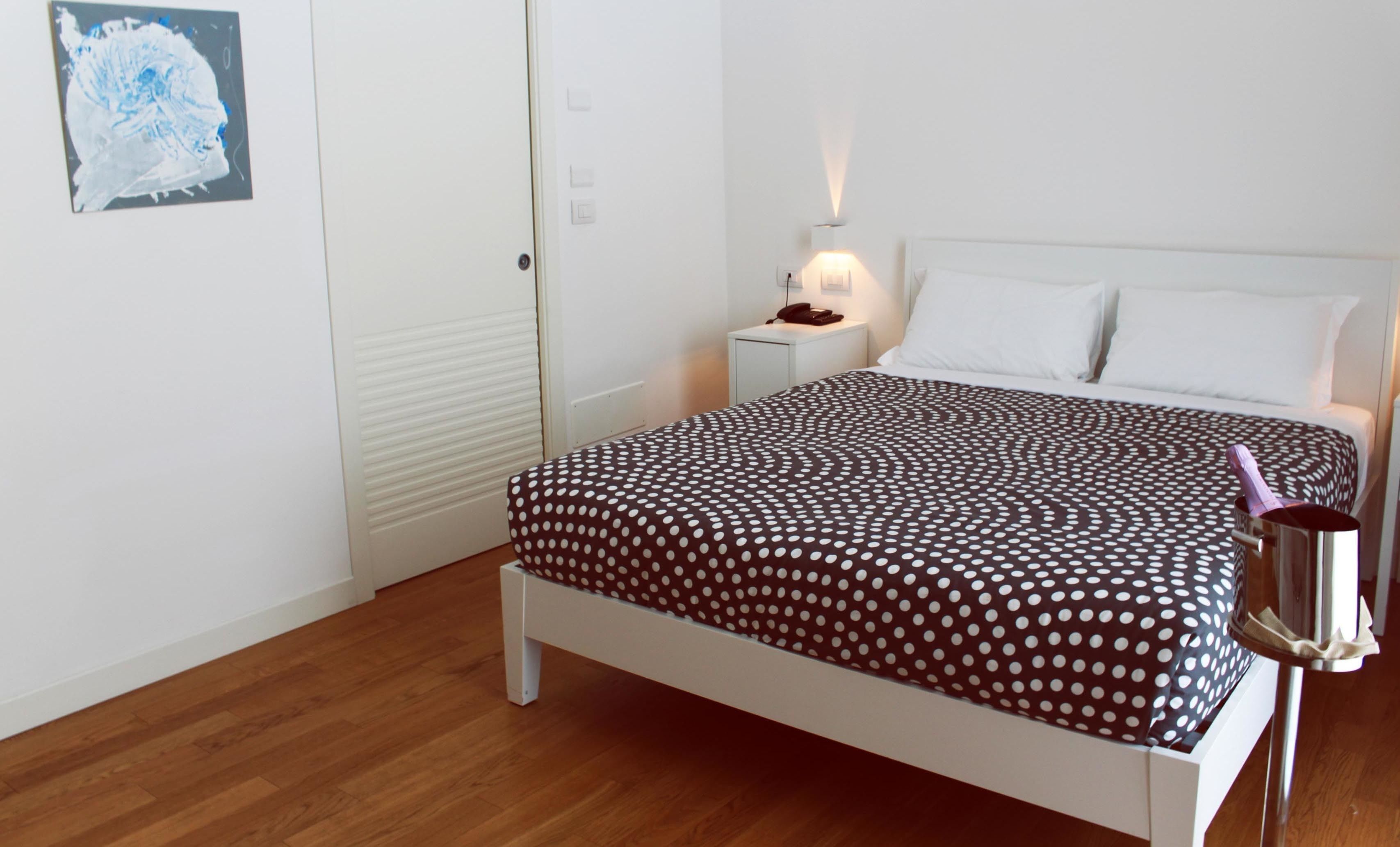 Ein ordentlich bezogenes Bett mit einem Punkte-Bettbezug, ein Nachttisch mit einer Lampe und ein Bild an der Wand.
