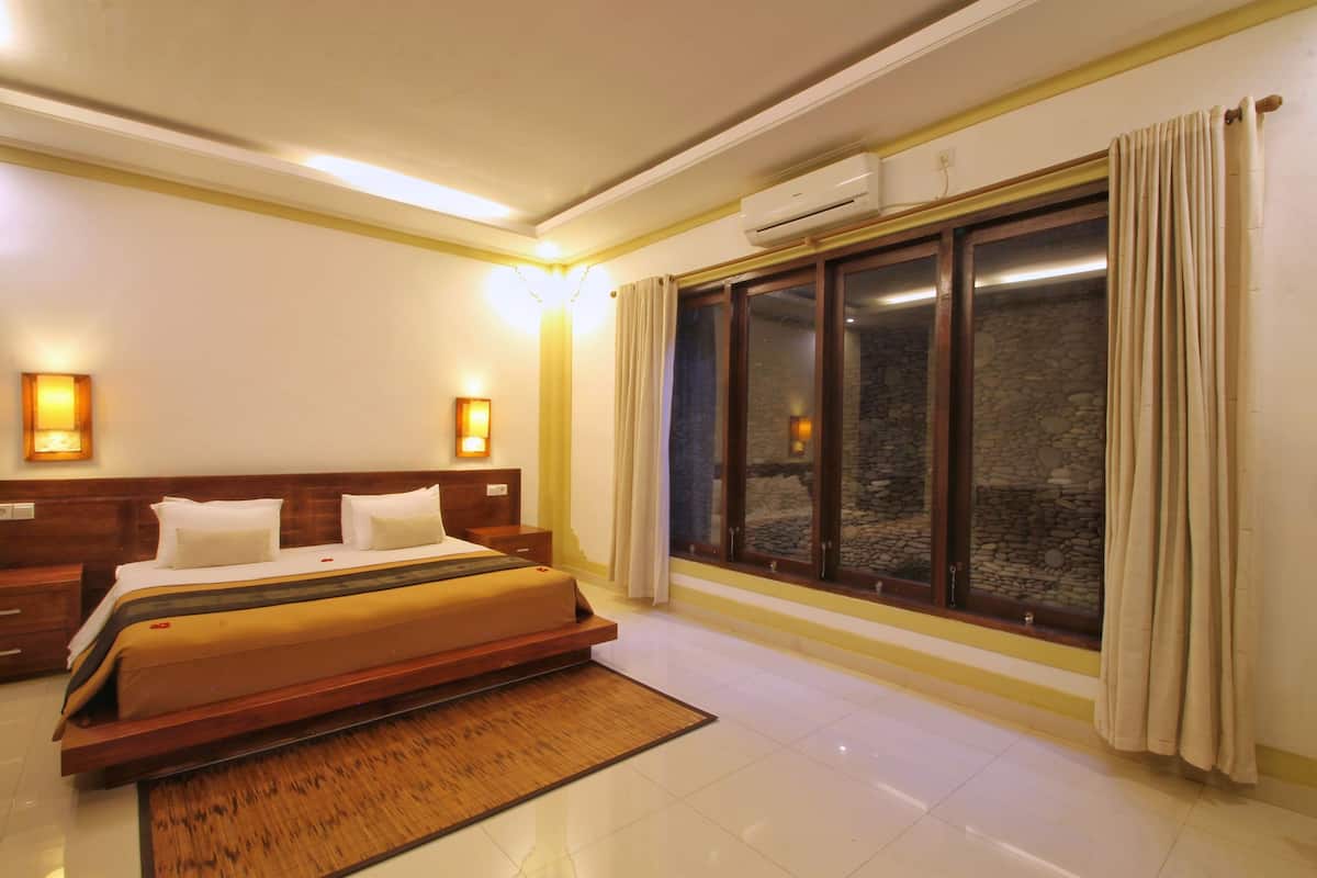 Una habitación de hotel con una cama grande, un ventanal con cortinas, un equipo de aire acondicionado y luces fijadas en la pared.