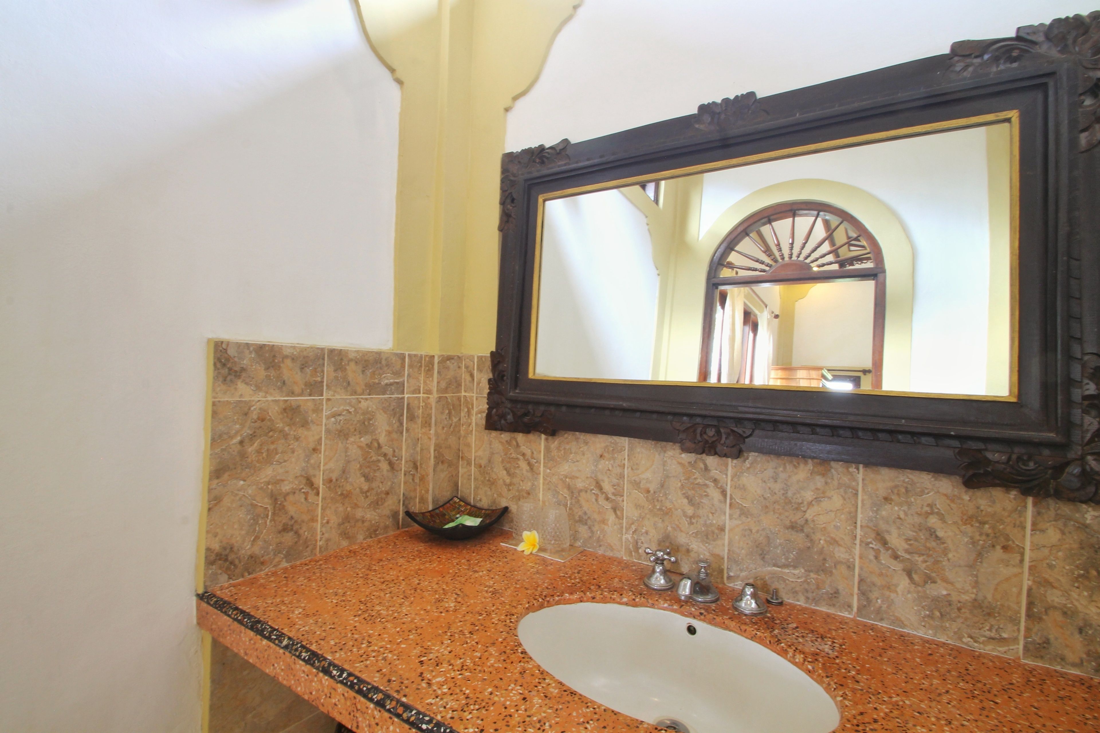 A bathroom with a granite countertop, a white sink, a mirror with an ornate frame, and a small decorative bowl on the counter.