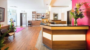 Un hall d’hôtel moderne avec un comptoir d’accueil, un espace salon et un grand lit en arrière-plan.