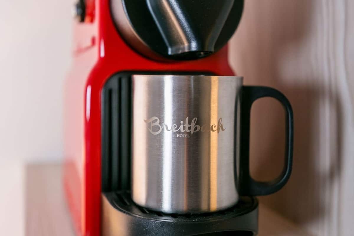 A red and silver coffee machine with a handle and a metallic base, labeled 'Breitbach HOTEL.'