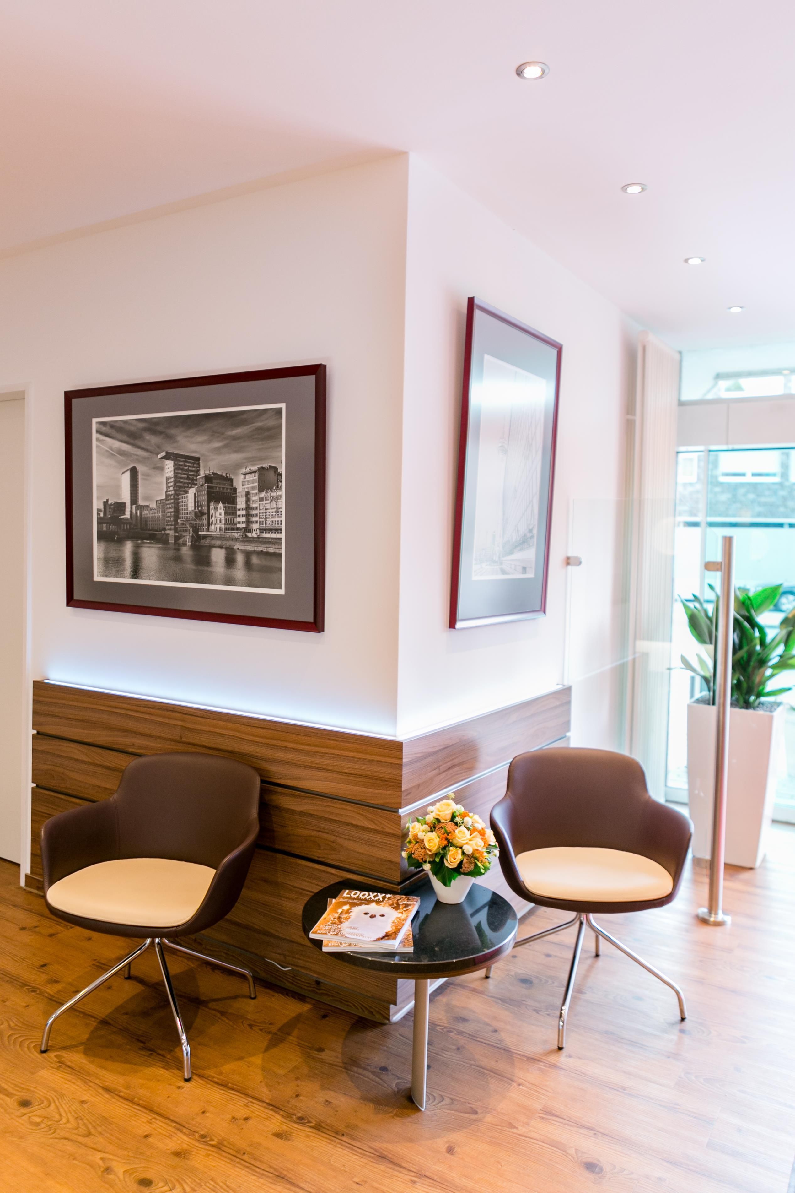 A reception area with two brown chairs, a small table with a magazine and a vase of flowers, and two framed pictures on the wall.